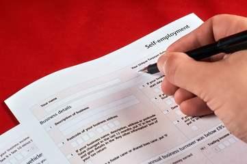 human fills self employment tax form on red velvet background