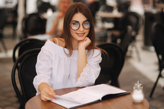 Stylish lady sits in cafe in centre of city and look at the menu. Sunny weather and codl drink. Girl in sunglasses chooses what to order