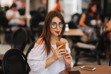 Stylish happy young woman wearing white shirt .She holds coffee. portrait of smiling girl in sunglasses