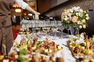 Bartender pouring champagne or wine into wine glasses on the table in restaurant. solemn wedding...