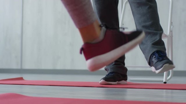 Unrecognizable female fitness trainer and her male client standing on yoga mats and doing ankle rotation exercise while warming up before workout