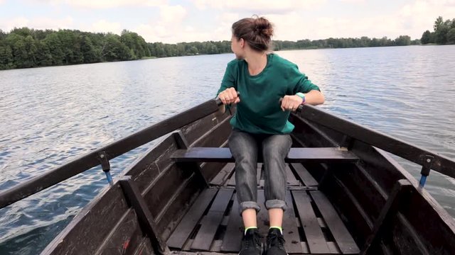 A young beautiful woman is sailing on a boat on the lake. A strong woman paddles with oars.