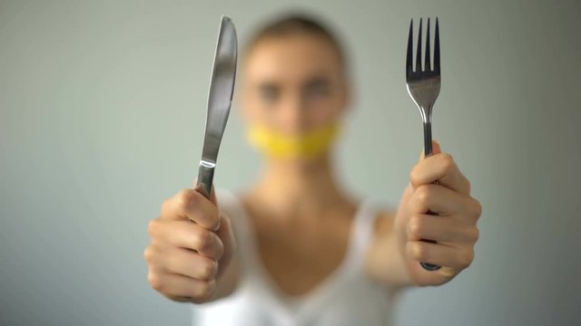Girl holding fork and knife, mouth closed with tape-line, food restriction