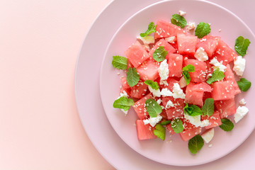 Summer watermelon salad with feta cheese, sesame seeds and mint leaves on pink plate. Healthy eating concept