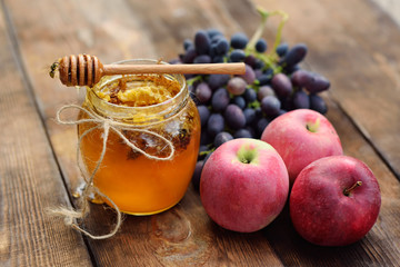 The wasps fly around the jar with honey, grapes and apples on a wooden background