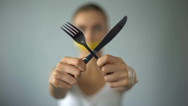 Woman crossing fork and knife, mouth closed with tape, self-restriction in food