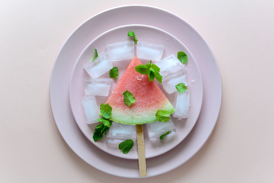 Frozen watermelon popsicles with mint on pink plate. Top view