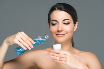 portrait of smiling woman with bare shoulders holding mouthwash isolated on grey - obrazy, fototapety, plakaty