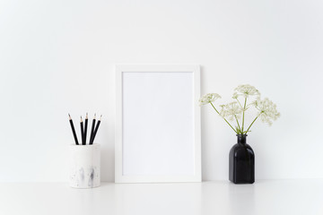 Stylish white portrait a4 frame mock up with a wild host in black vase and black pencils near white wall. Mockup for quote, promotion, headline, design. Template for small businesses, social media