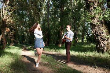 young couple walking in the forest, playing guitar and dancing, summer nature, bright sunlight, shadows and green leaves, romantic feelings