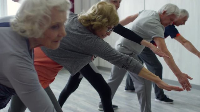 PAN of elderly people in sportswear standing in line and doing side bend exercise, then holding their balance during yoga class