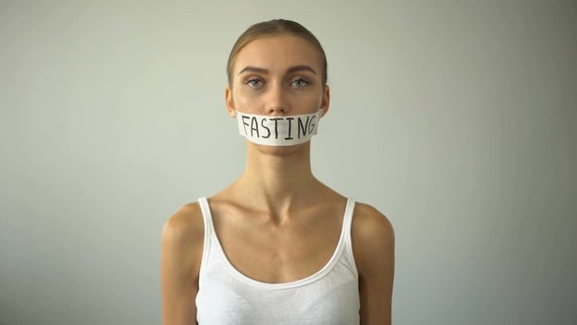 Fasting word written on taped mouth of upset anorexic model, self-destruction