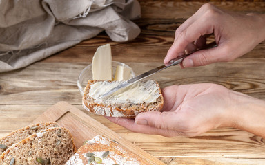 Female hands spread butter on a sandwich. Homemade rye bread on a wooden table