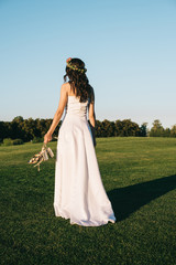 Fototapeta na wymiar back view of tender young bride holding shoes and walking on green lawn