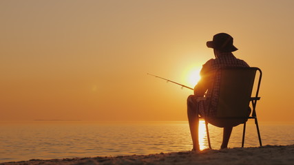 A young man is sitting on the seashore, fishing. Relaxing in the open air