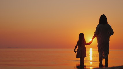 A pregnant woman with a daughter is standing on the beach at sunset. Waiting for the second child