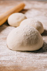 selective focus of raw dough for pizza and rolling pin on tabletop
