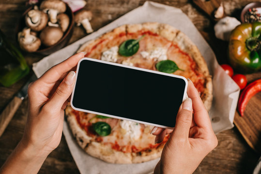 Cropped shot of food blogger taking picture of cooked pizza on baking paper on wooden surface