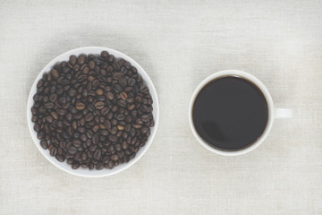Good morning! Coffee beans in a white saucer. Coffee cup. Light textured background, toned photo. View from above. Copy space
