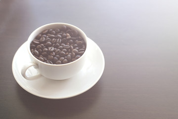 White mug with coffee beans. Wooden table. Toned photo. Copy space