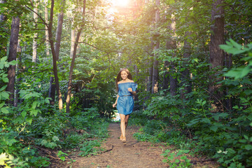 Naklejka na ściany i meble Nature, people and lifestyle concept - Beautiful young woman in dress runing in the summer forest