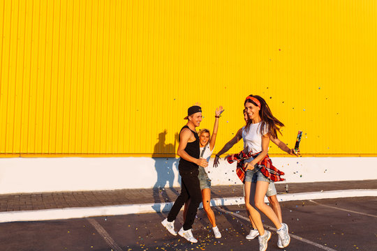 Beautiful cool young jump with confetti on a yellow background, a group of young people celebrating and having fun, summer mood, friends walking in the city in place, lifestyle