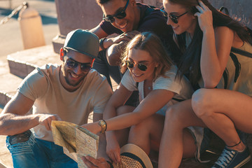 Group of friends on vacation with map sitting at town square and having good time.