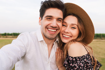 Lovely smiling couple man and woman dating, and taking selfie together, while walking outdoor through field