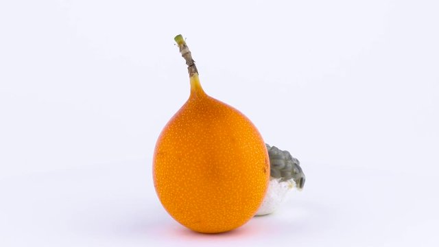 One whole sweet granadilla fruit and its pulp. Slowly rotating on the turntable isolated on the white background. Close-up. Macro.