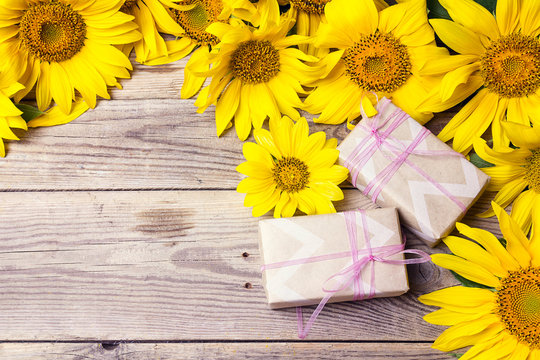 Background with yellow sunflowers and gift boxes on wooden table.
