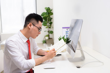 Happy businessman with book in hand looking at computer monitor in office