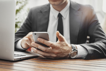 Close up of businessman looking at mobile phone and working with laptop.