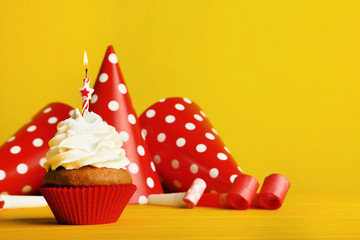 Cupcake with candle, paper caps and blowers on yellow background