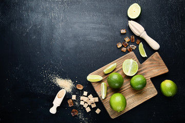 Ripe limes with mint leafs and sugar on black wooden table