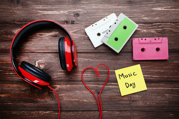 Headphones with cassette tapes and inscription Music Day on wooden table