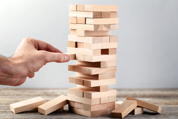 Male hand playing wooden blocks tower game on grey background
