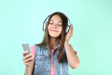 Young girl with headphones and smartphone on mint background