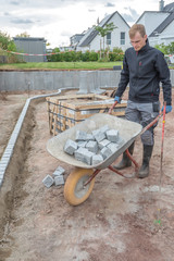 Mann schiebt Schubkarre mit Granitkantensteinen