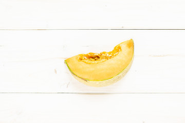 One slice of fresh melon cantaloupe variety flatlay on grey wood