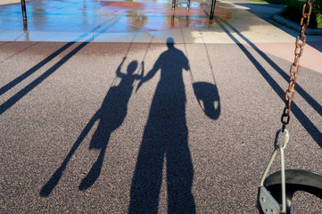 Shadow of father and child playing on a swing