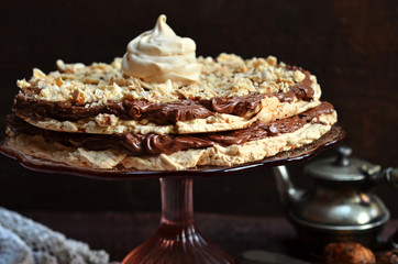 Meringue cake with chocolate cream on a glass plateau on a wooden background