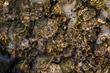 Sharp sea surface on the pebbles beach reflecting sun rays.Use for background.