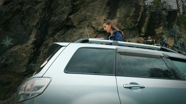 Female freelnacer is working with laptop on the roof of her car