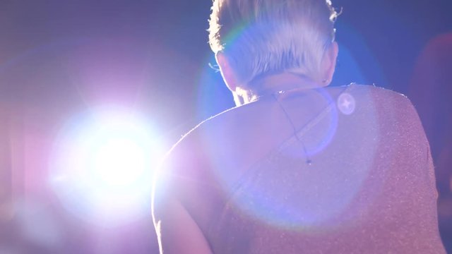 music concert, beautiful young singer on stage with microphone performs a song in lighting