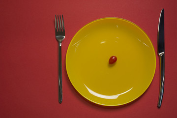 Diet concept plate top view. Cherry tomato on yellow empty plate with fork and knife on red background