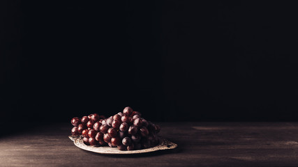 fresh ripe red grapes on vintage plate on wooden table on black