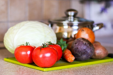 Ingredients for ukrainian traditional borsh on the green cutting desk with cooking pot at background. Selective focus.
