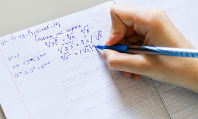 Close-up shot of student hand writing down math formulas of square roots in the copybook with...