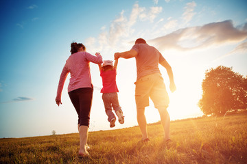 girl with mother and father holding hands on the nature. Child with parents outdoors