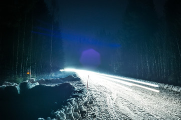 Car headlights on a winter road in the forest, on long exposure
